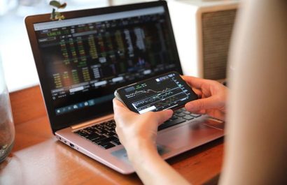 Female hand with smartphone trading stock online in coffee shop , Business concept