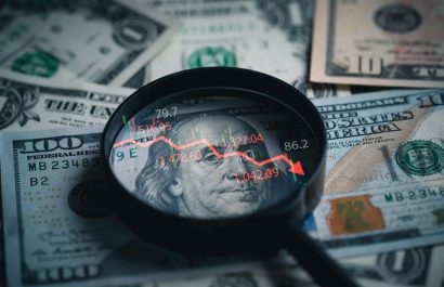 Red down arrow inside of magnifier glass and USD dollar banknote for United States of America or USA economic recession concept.